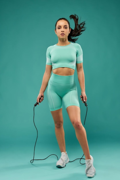 Attractive young woman in sportswear using skipping rope