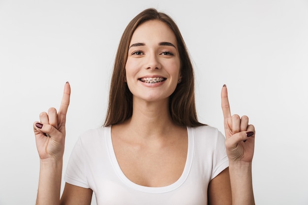 Attractive young woman standing isolated over white wall, pointing at copy space