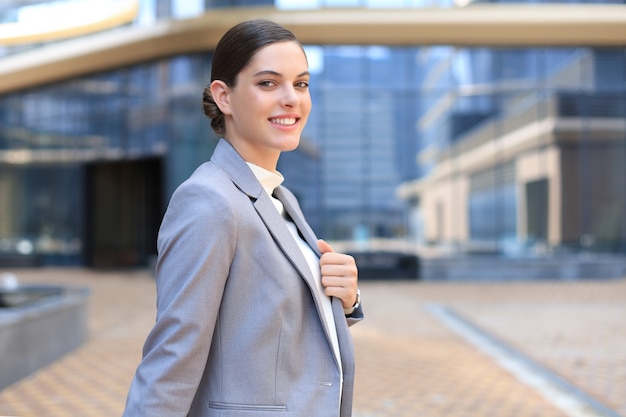 Attractive young woman in suit looking at camera and smiling while standing outdoors.