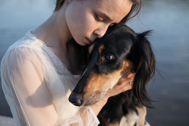 Attractive young woman in white dress holding saluki dogs face with love. Face to face. persian greyhound. Pets care concept. Love and friendship between human and animal.