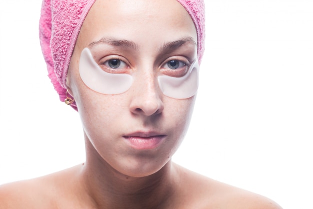 Attractive young woman with white patches under the eyes and a pink towel on her head isolated on. Closeup portrait. Skin care