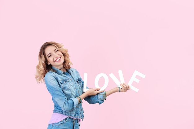 Attractive young woman with word LOVE on color background