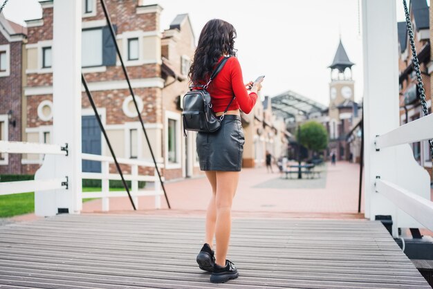 Attrative dark-haired tourist girl walking through the old town street with mobile phone in hands browsing maps application