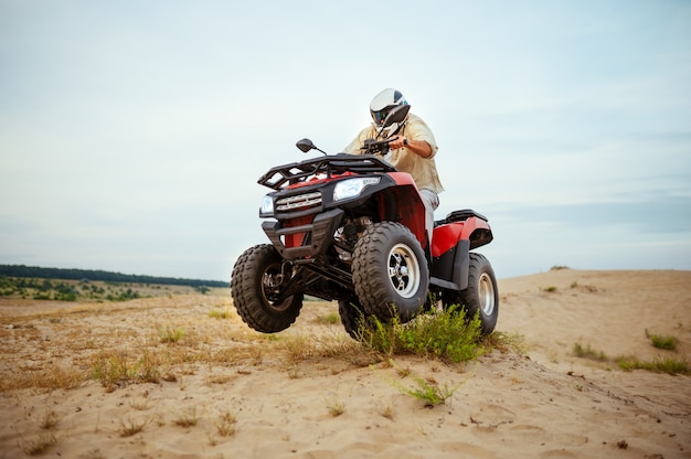 Atv racer in helmet, downhill riding in desert sands, action view. Male person on quad bike, sandy race, dune safari in hot sunny day, 4x4 extreme adventure, quad-biking