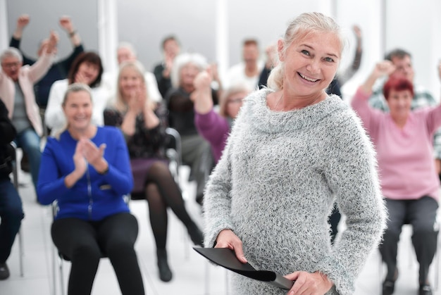 Audience at seminar applauding brunette smiling woman holding documents