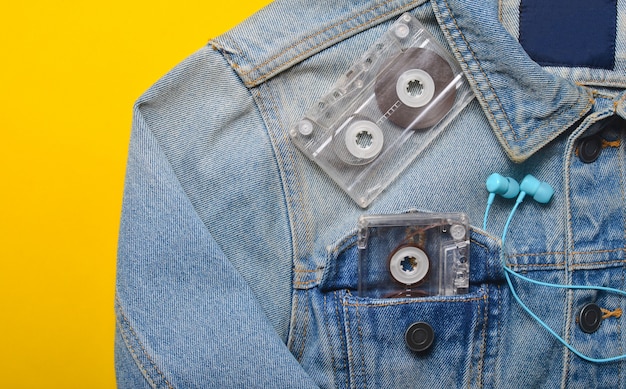 Audio cassette and headphones in the pocket of a hipster jeans jacket on a yellow background. Entertainment 80s. With music in life.