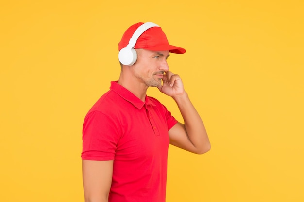 Audio guide Man in headphones on yellow background Incoming call Worker in uniform with earphones Assistant call center help find solution Guy call service worker Man listen music headphones