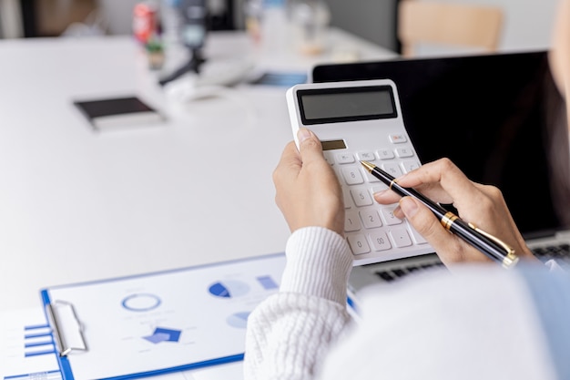 Photo the auditor is pressing the white calculator, she is the company's auditor is responsible for checking all the company's income and expenses documents for accuracy. accounting audit concept.