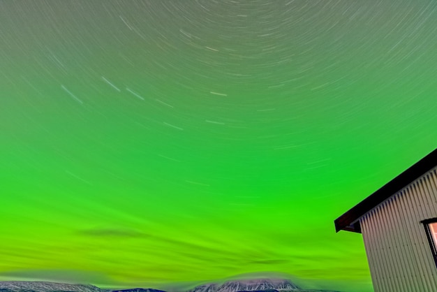 Aurora borealis lights river and house edge long exposure