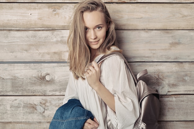 Authentic blonde young girl with silver backpack over wood wall