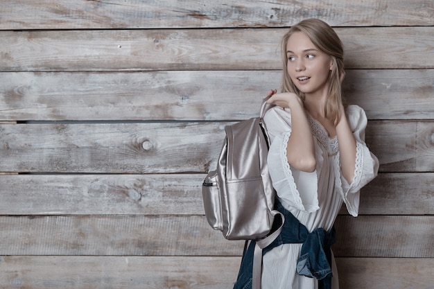 Authentic blonde young woman with silver backpack over wood wall