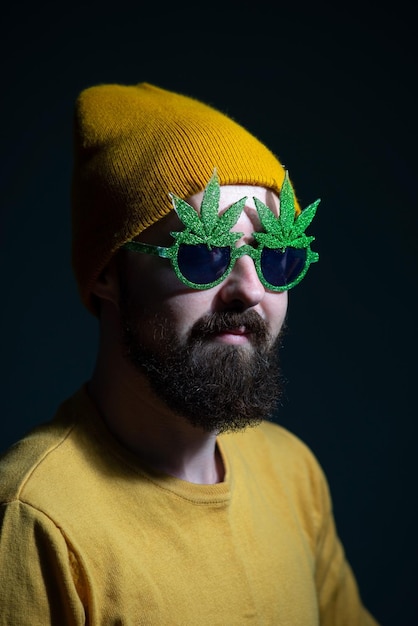 Authentic portrait of a cheerful guy in sunglasses marijuana on a dark background