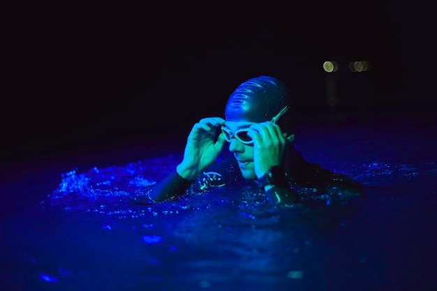 authentic triathlete swimmer having a break during hard training on night neon gel light