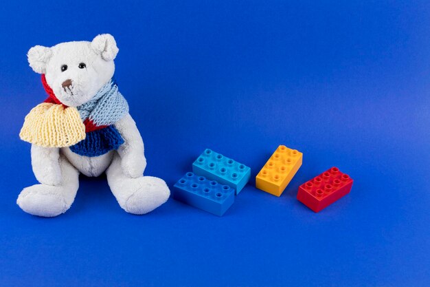 Autism awareness background Teddy bear with jigsaw pattern colors knitted scarf sitting on blue background Copy space