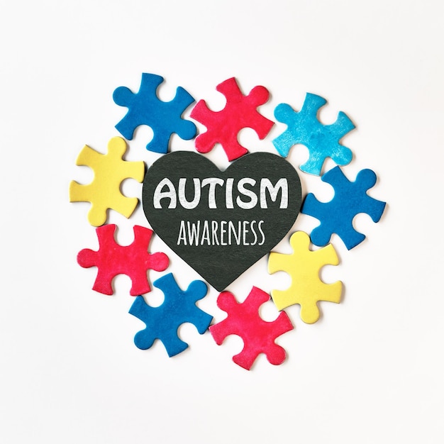 Autism campaign symbols Colorful puzzle pieces around blackboard stone heart with words Autism Awareness written in chalk Flat lay top view square composition