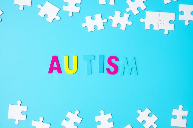 AUTISM text with white puzzle jigsaw pieces on blue background. Concepts of health, Autistic Spectrum disorder and world Autism awareness day