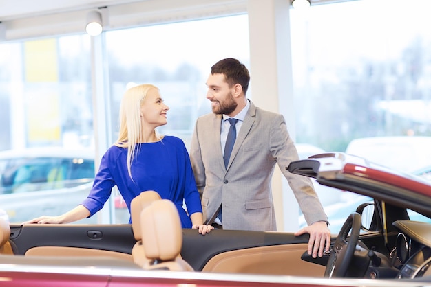 auto business, car sale, consumerism and people concept - happy couple buying car in auto show or salon