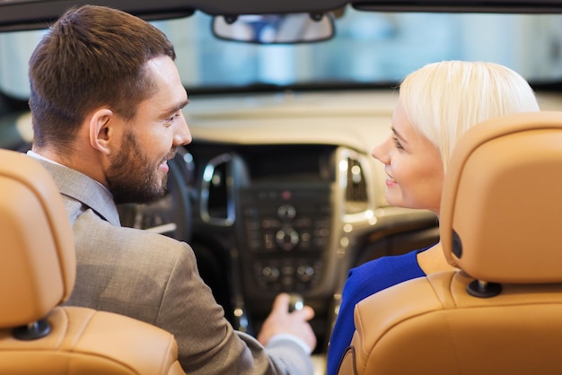 auto business, car sale, consumerism and people concept - happy couple sitting in car at auto show or salon