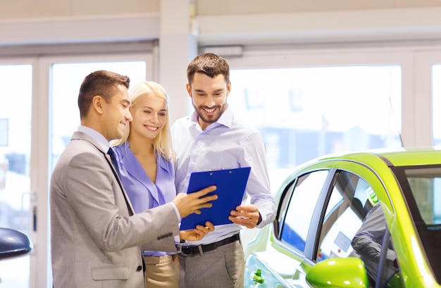 auto business, car sale, technology and people concept - happy couple with car dealer in auto show or salon