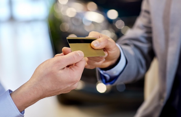 auto business, sale and people concept - close up of customer hand giving credit card to car dealer in auto show or salon