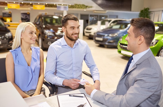 auto business, sale and people concept - happy couple with dealer buying car in auto show or salon