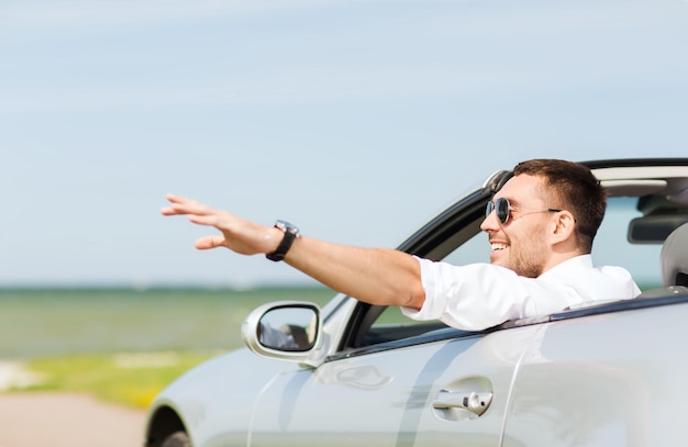 auto business, transport, leisure and people concept - happy man driving cabriolet car and waving hand outdoors