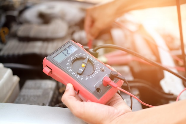 Auto mechanic check car battery voltage by voltmeter multimeter 