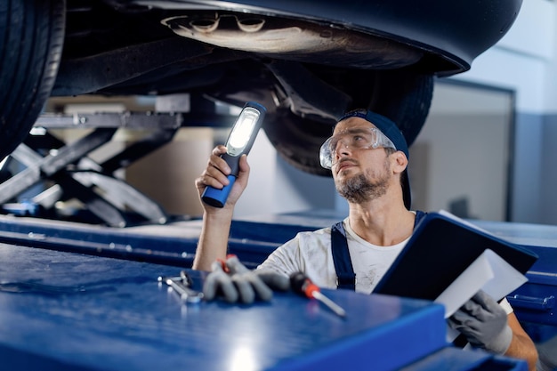 Auto mechanic examining chassis of a vehicle with a flashlight in a workshop