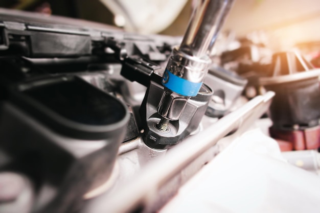 The auto mechanic is fastening the bolt of car ignition coil with the socket wrench