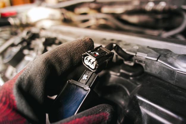 The auto mechanic is unplugging the ignition coil of the car engine in the engine compartment