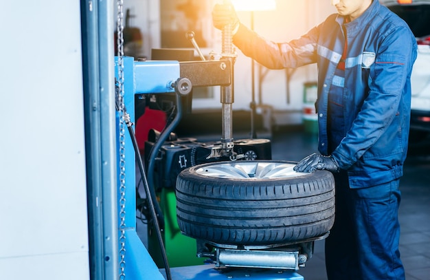 Auto mechanic loading automobile car wheel at tyre fitting machine during tire replacing auto servic