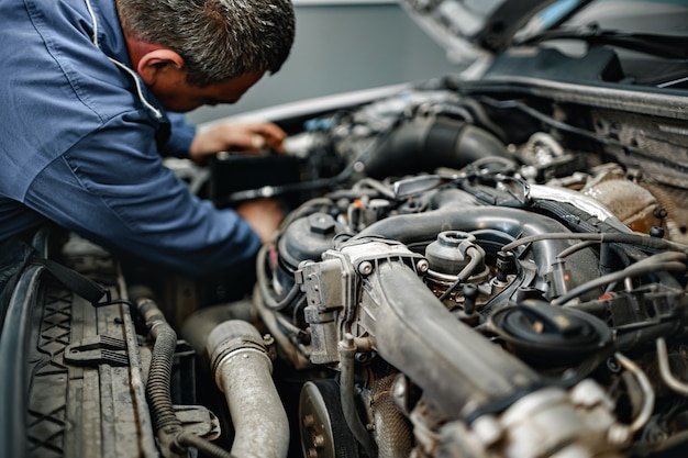 Auto mechanic man checks car engine under the hood close up