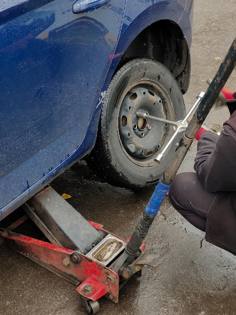 The auto mechanic sits down next to the wheel of the car the bolts on it with a special key