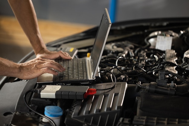 Auto mechanic uses laptop while conducting diagnostics test modern car service computer diagnostics