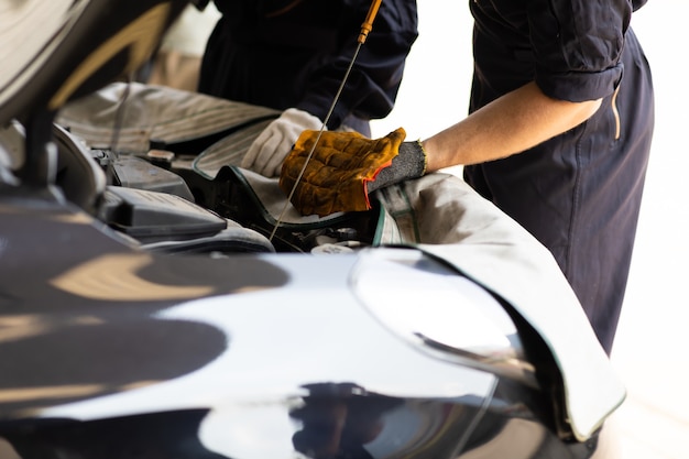 Auto mechanic worker checking oil level in car engine. Car maintenance and auto service garage concept.