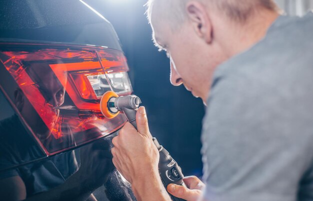 Auto mechanic worker polishing car at an automobile repair and renew service station shop by power b