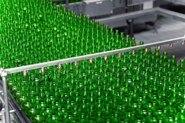 Automated conveyor line in a brewery. Rows of green glass bottles on a conveyor belt.