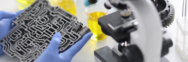 Automatic transmission lies in rubber gloves on table with microscope and test tubes in chemical laboratory closeup. Quality control of engine oils concept.