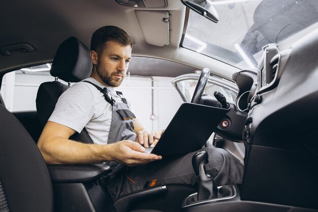 Photo automotive mechanic running diagnostics software on computer mechanic sitting in car and working on laptop while doing vehicle diagnostic test in auto service garage