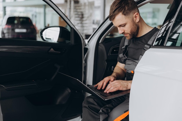 Photo automotive mechanic running diagnostics software on computer mechanic sitting in car and working