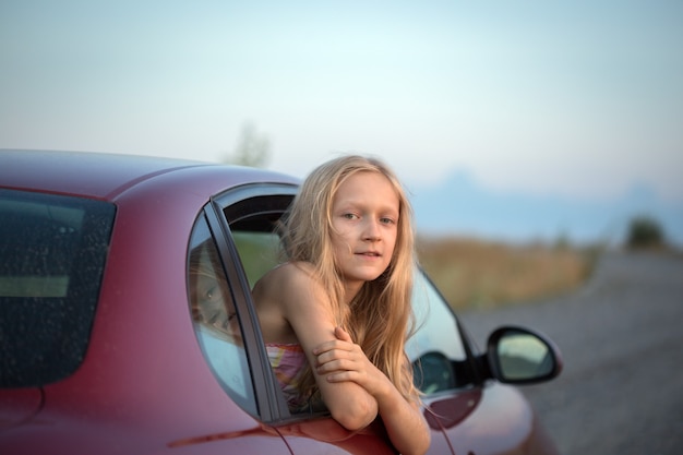 Autotravel with children. happy smiling little girl looking out the car window and sunset at the background