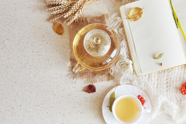 Autumn aesthetic organic linden tea in teapot with cup of tea, mock up notebook.Cozy atmosphere home