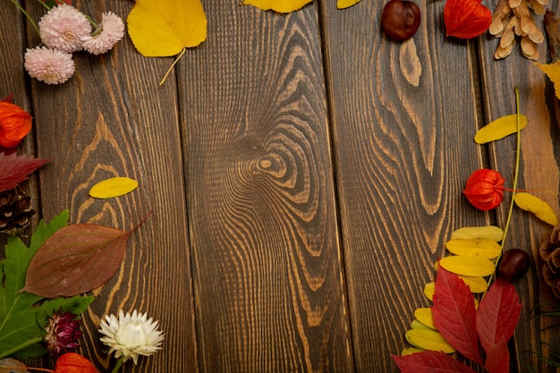 Autumn background. Bright orange berries, very flowers and leaves on a brown wood background.