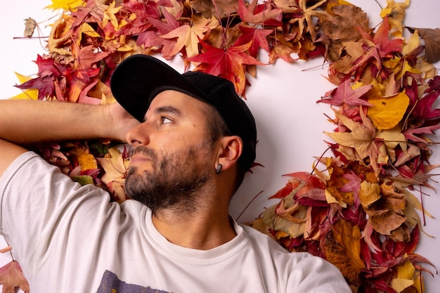 Autumn background man in a black cap in a studio lying on colored leaves