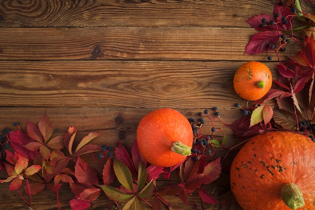 Autumn background - orange pumpkins with red leaves on a wooden table. Top view, copy space and thanksgiving concept..