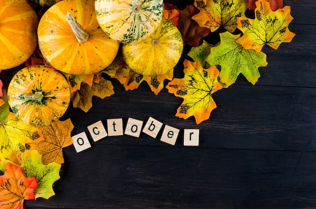 Autumn background with decorative pumpkins, leaves and text October on a dark old wooden table