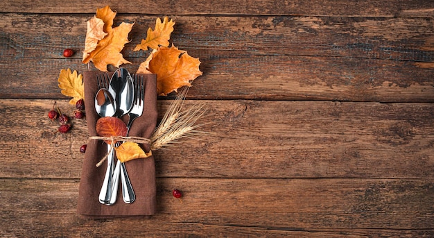 Autumn background with napkin cutlery and autumn leaves on a wooden background with space to copy