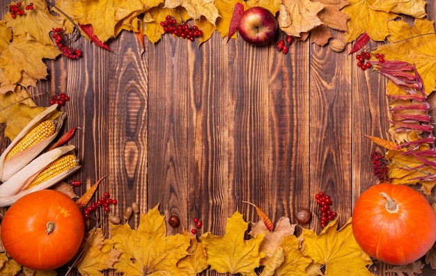 Autumn background with yellow maple leaves, pumpkins, red apples and berries.