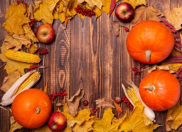 Autumn background with yellow maple leaves, pumpkins, red apples and berries.