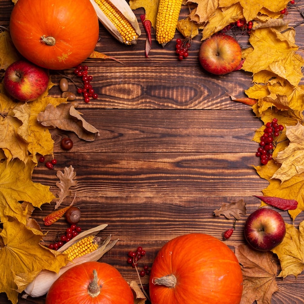 Autumn background with yellow maple leaves, pumpkins, red apples and berries.